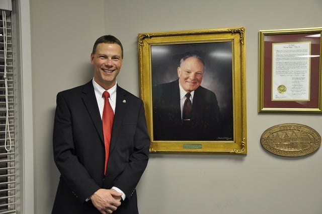Avondale Estates City Manager Clai Brown stands next to a portrait of his father, former city manager and police chief Dewey Brown. Photo by: Dan Whisenhunt