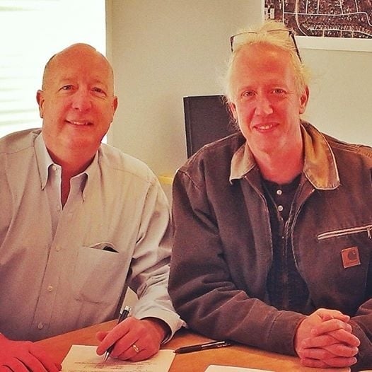 Mayor Ed Rieker, left, and Watts Whiskey Distillery owner Tim Watts, right, sign paperwork related to the opening of the distillery at Tudor Square, a building Rieker owns. Photo distributed by the city of Avondale Estates. 