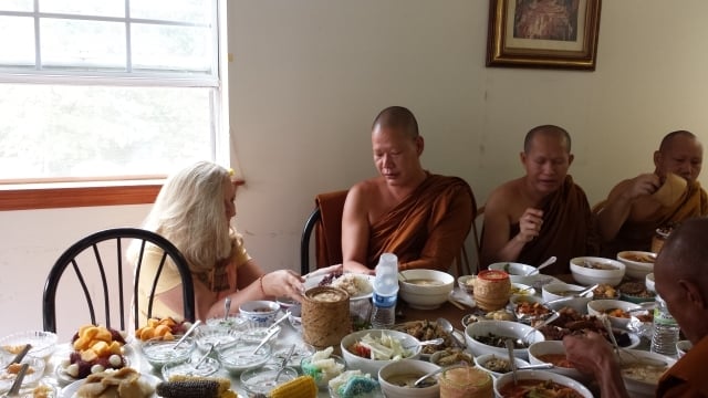 Melissa O'Shields places a plate of food on a cloth in front of a monk. Photo by Dena Mellick