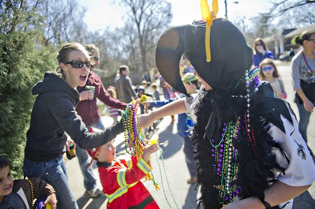Eddie Galatas (right) hands a pile of beads to Courtney Goetzel and her son Miles as they watch the Mead Road Mardi Gras parade pass by on Saturday, Feb. 7, 2015. Photo by Jonathan Phillips