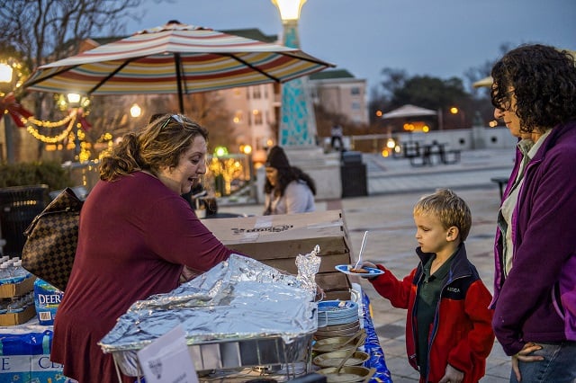 Carol Epstein (left) hands Andrew Sugarman and his mother Elysa a potato latke during the Chanukah celebration in Decatur Square on Thursday. Photo: Jonathan Phillips