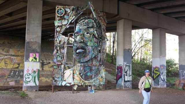 A Trees Atlanta volunteer tells a tour group from the Caring for Creation conference about artwork by William Massey called "The Art of Reconciliation." The work, located on the BeltLine, is made from old junk from the streets of Atlanta. Photo by Dena Mellick