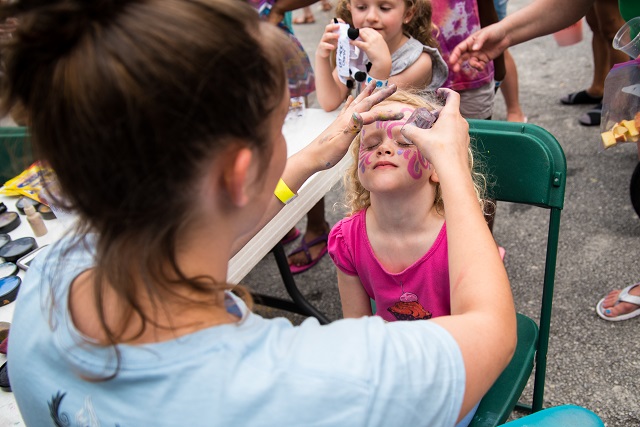 Anna Gieger sprinkles glitter on Maggie Fair at the face painting table.
